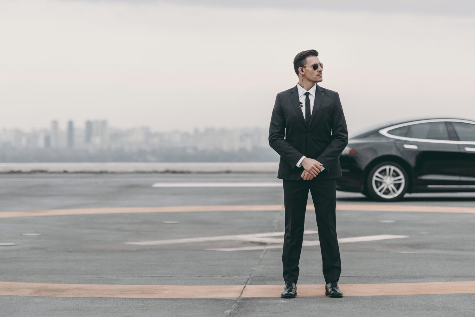 Professional bodyguard in suit beside luxury car