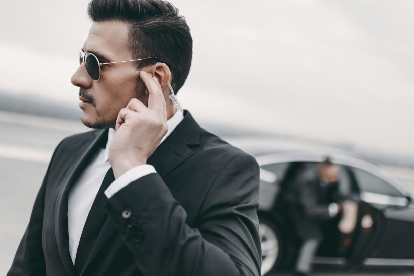 Bodyguard in suit adjusting earpiece by car